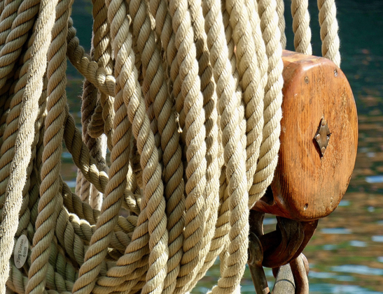 Die Nahaufnahme zeigt detailreich eine Ansammlung von Seilen und Tauwerk, die sich neben einem maritimen Taljenblock an Bord eines Traditionsseglers befinden.