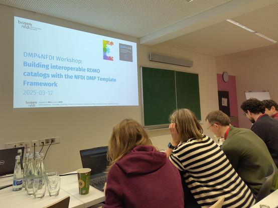 Picture of the auditorium and the first slide of the DMP4NFDI Workshop.