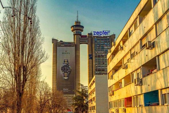 A bustling city street in Belgrade featuring a tall building prominently in the background, showcasing urban architecture and activity.