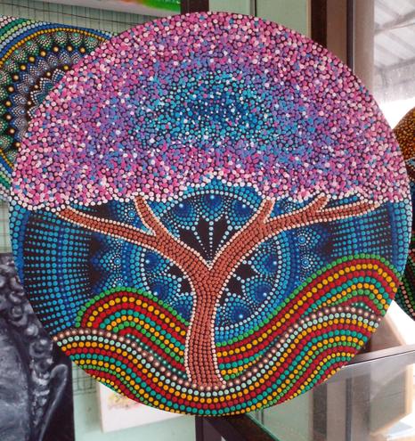 a tree on a wavy ground, a blue mandala in the background, the leaves of the tree are pink and white and blue 