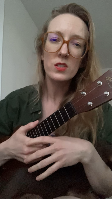 Sage, a white lady in her mid thirties, sits and sings and plays her ukulele