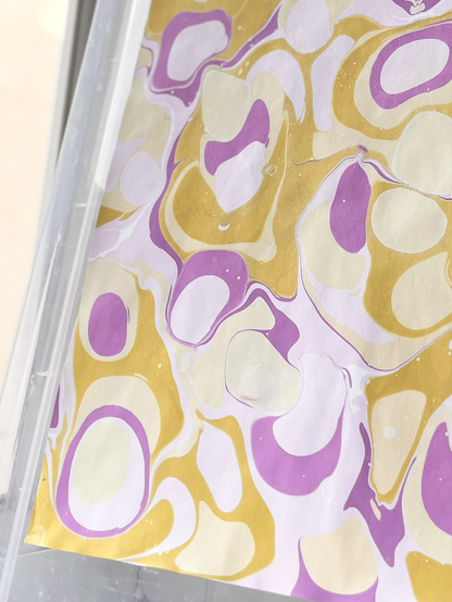 Nahaufnahme von marmoriertem Papier mit Blobs aus lila, fliederfarben, gelb und hellgelb.