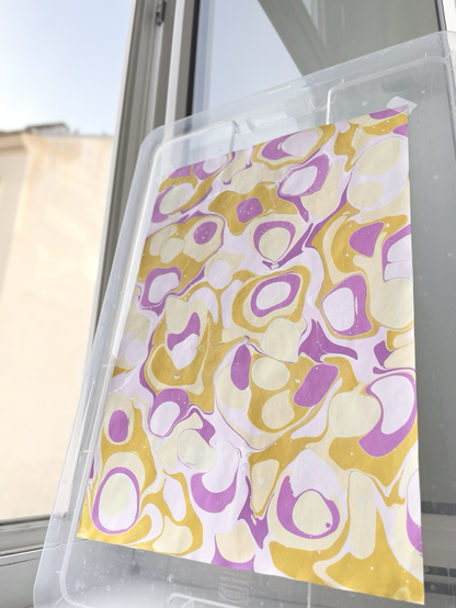 Aufnahme von weiter entfernt von marmoriertem Papier mit Blobs aus lila, fliederfarben, gelb und hellgelb.