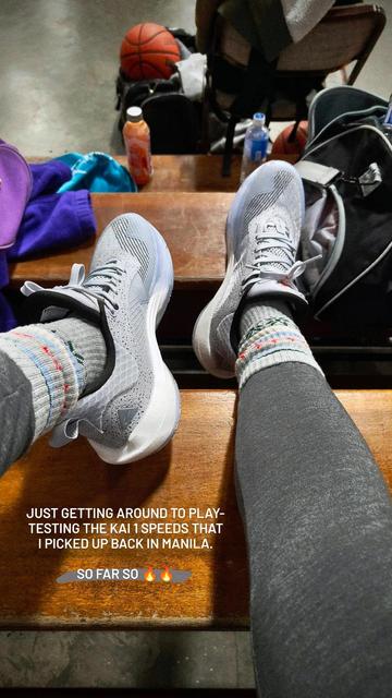 Close-up photo from a first-person perspective of a new pair of grey Anta KAI 1 Speeds worn with matching colored socks and base layer at a basketball gym.