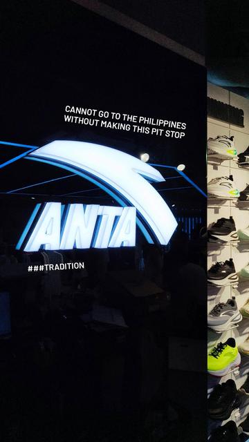 Photo of a large, lit up ANTA sign at one of their store locations in Manila, Philippines; a wall of shoe models on display can be seen off to the side.