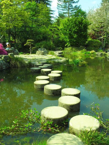 Une chemin fait de poteaux émergeant d'un plan d'eau dans un jardin public typé japonais