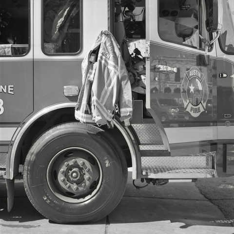 A black and white film photo. A firefighter’s coat hangs on the side of Engine 13 fire truck in downtown Austin, Texas. Wednesday, February 26, 2025.