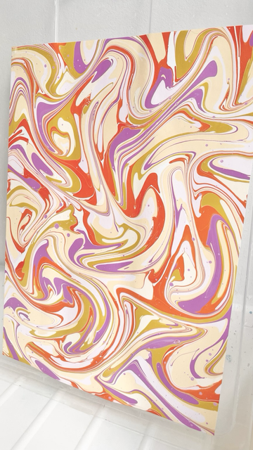 Schwungvolles marmoriertes Muster auf Papier aus lila, gelb und orange.