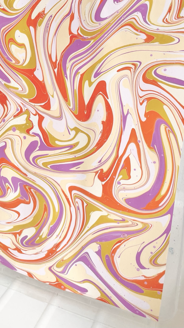 Schwungvolles marmoriertes Muster auf Papier aus lila, gelb und orange.