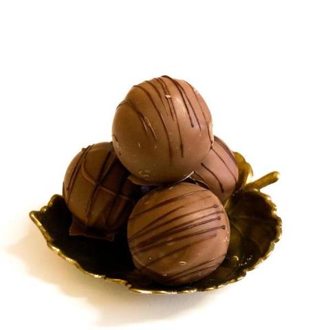 4 runde Pralinen aus Vollmilchschokolade und mit einem Dekor aus dunklen Schokoladenstreifen liegen auf einem messingarbenem blattförmigen Schälchen vor weißem Hintergrund.