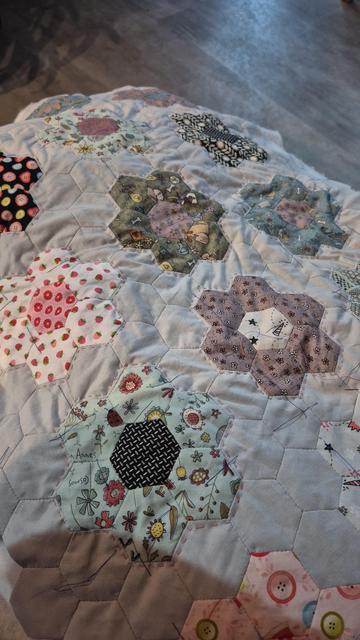 Ausschnitt eines in EPP (english paper piecing)Technik handgenähtem Kissen. Grauer Hintergrund, bunte Blumen gebildet mit buntem Stoff. Noch recht zerknittert gequiltet.