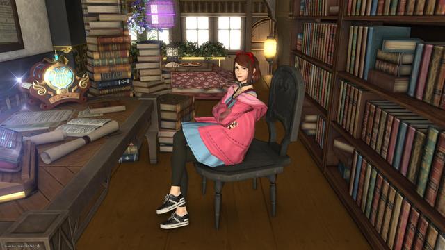 Esi sitting in Lia's upstairs library, surrounded by books stacked up high next to the desk and in shelves behind her.