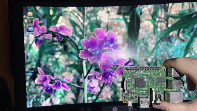 Raspberry Pi 3 board in my hand with ToaruOS running on it in the background monitor.