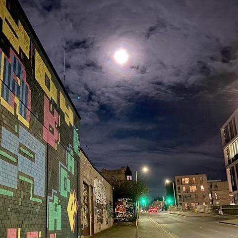 Colorful moonbow through thick clouds above two green lights and an 8-bit mural