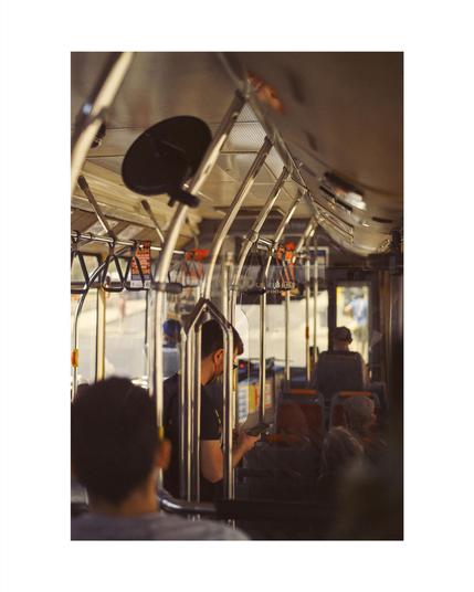 a man standing in a public bus, face hidden behind metal handles, other passengers sitting in the bus seats