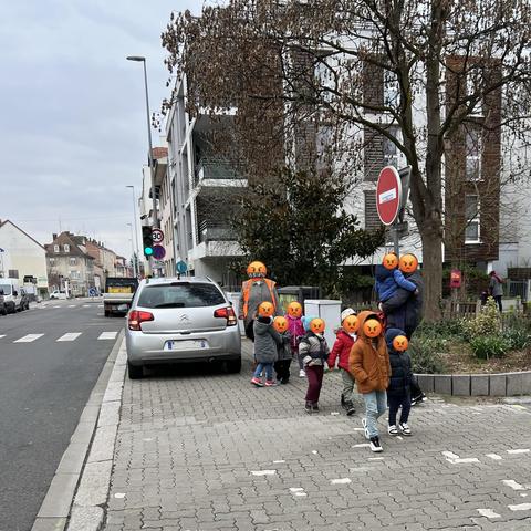 Une Citroën C3 grise stationnée sur le trottoir en face de la pharmacie, juste avant le feu. Un groupe d’enfants (scolaire) accompagné d’adultes se faufile un chemin.