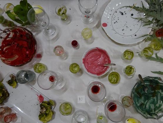 table vue de haut avec des restes de nourriture verts, roses, rouges dans des verres, des plats, des assiettes