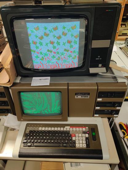 Auf dem Bild sind ein Farbbildschirm und ein Computer mit Grünbildschirm. Der Computer ist ein A5120 von robotron. Dieser ist in einen Braunton gehalten mit 3 fünfeinhalb Zoll Diskettenlaufwerken. 