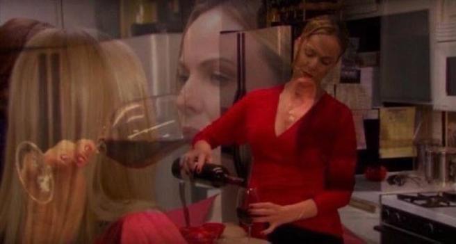 A woman in a red shirt is pouring red wine into a glass in a kitchen setting. The image has a soft, blurred overlay featuring another woman's face drinking wine, creating a dreamlike emotional effect.