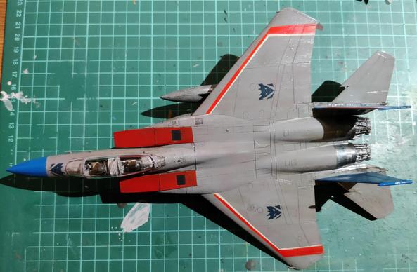 A grey-red-blue F-15E model viewed from top, with a once-cleaned up brown oil wash applied all over. The model is set on a well-worn green cutting mat, lying askew after the left landing gear came off.