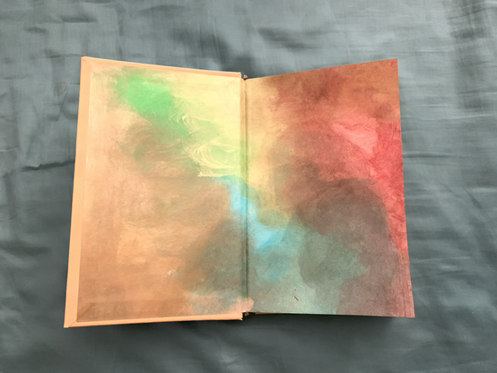 The book Ubik front cover has been opened to display the front end paper. The end paper is hand painted in bright and vibrant colors of yellow, green, blue, gold, copper, and red. The colors swirl like smoke, blending into each other. 