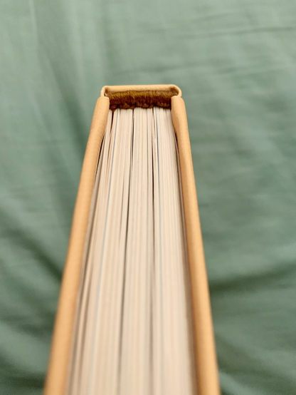 Looking at the top edge of the book, we can see a close up of the hand sewn endband that sits at the top of the book’s spine. The endband is sewn in shiny brown cotton thread.