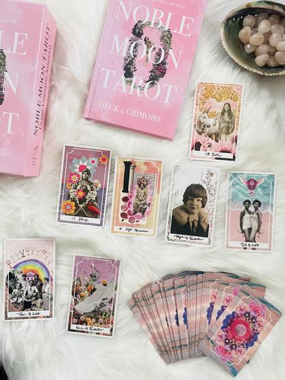 Spread of tarot cards and hard back book, making up the Noble Moon Tarot Deck & Grimoire. The cards are LGBTQ2SIA+ and femme empowering with various ages, races, and body types in joyful expressions. 