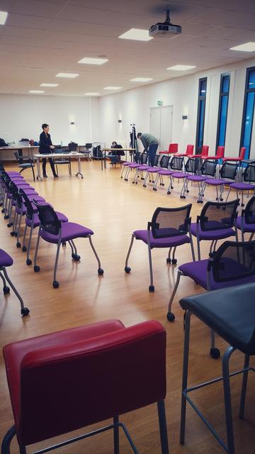 Salle de classe - set pour le jeu du théâtre forum - chaises en U devant une table et trois chaises - dans le fond l'équipe se prépare - Mary Léaument, Agathe Cardona et Cyrille Berthe.
