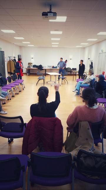 Salle de classe - set pour le jeu du théâtre forum - chaises en U devant une table et trois chaises - qui se remplissent petit à petit des participant-es en attendant le début de l'atelier.