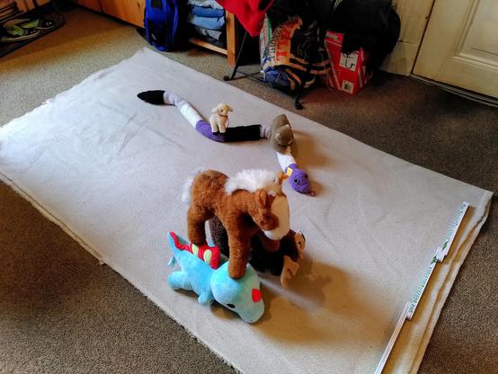 Ein Wettrennen unter Plüschtieren. Elch Gunvald und Spinosaurus Zilla laufen nebeneinander und tragen gemeinsam Pferd Angelika. Auf der Bahn daneben reiten das kleine Schaf Lily und Katerchen Rainer auf der Schlange Anna Konda, die im Rennen rund eine Schlängelwindung zurückliegt. 