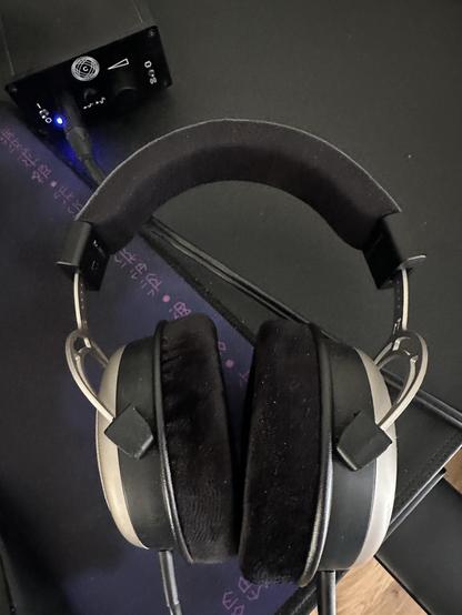 A pair of Beyerdynamic T1 headphones lying on a desk near to a headphone amp