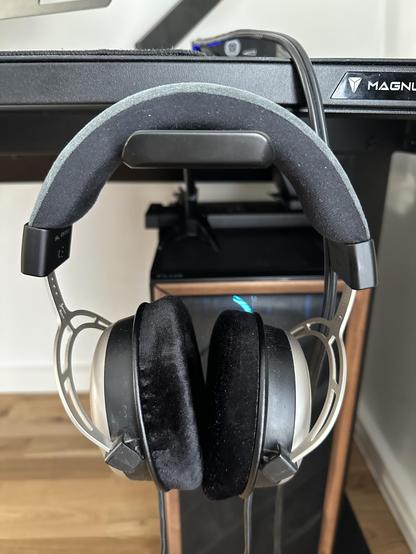 A pair of Beyerdynamic T1 headphones hanging from a headphone holder at the edge of the desk 
