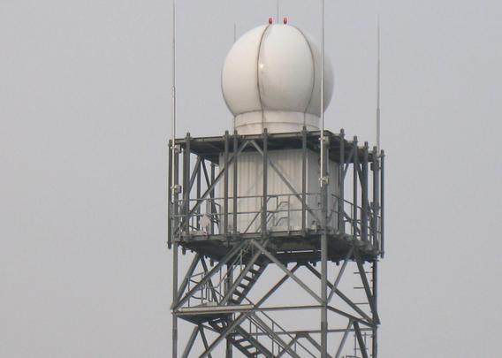 Detailaufnahme des Wetterradars. Der obere Teil des Turms, innen befinden sich Treppen, darüber der Container und ganz oben der Radom mit zwei roten Leuchten als Hindernisbefeuerungslicht.