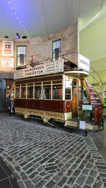 A horse-drawn tramcar, minus the horses. Livery cream and brown, with the words 'Glasgow Corporation Tramways' at the bottom. It has an open desk and a mannequin in period dress sits in the middle.