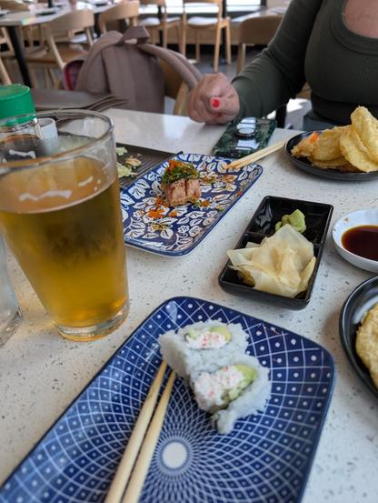 A table with Sapporo beer, two sushi rolls, and tempura vegetables