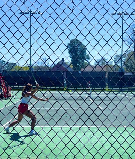 A UL Lafayette women tennis player is in full prep for a swing to defend a serve, as seen through a chain linked fence. 