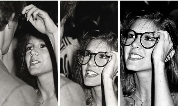 Actress Carrie Fisher trying on Peter Weller's glasses. She looks beautiful. Images are in blac k and white