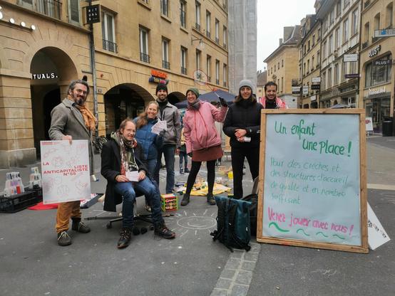 Action en ville de Neuchâtel pour des places de crèche en nombre suffisant. Sept candidates et candidats de solidaritéS présentent le programme du partit pour les élections cantonales 2025. Sur un panneau on peut lire: Un enfant une Place ! Pour des crèches et des structures d’accueil de qualité et en nombre suffisant.