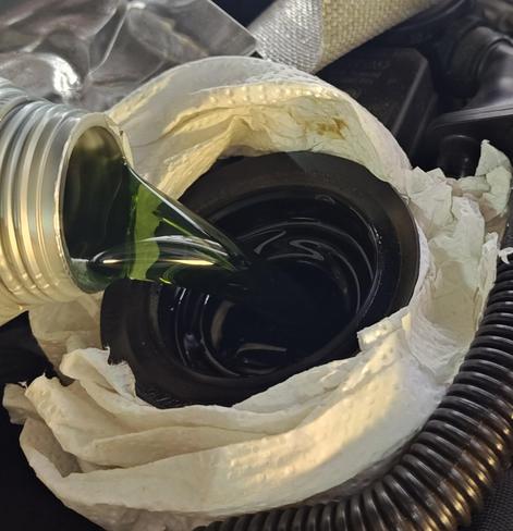 Engine oil being added to a car. There is a white paper towel around the filler, and as the oil pours over you can clearly see that it has a green tint, as opposed to most oil which is yellow/honey colored