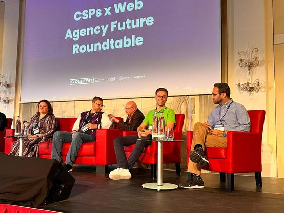 Five panelists are seated on stage in red chairs, discussing at the CSPs × Web Agency Future Roundtable at CloudFest. A large screen in the background shows the event title and sponsor logos. Ronny Marx, Commercial Director at Syde, is sitting in the center, wearing a green polo shirt and smiling.