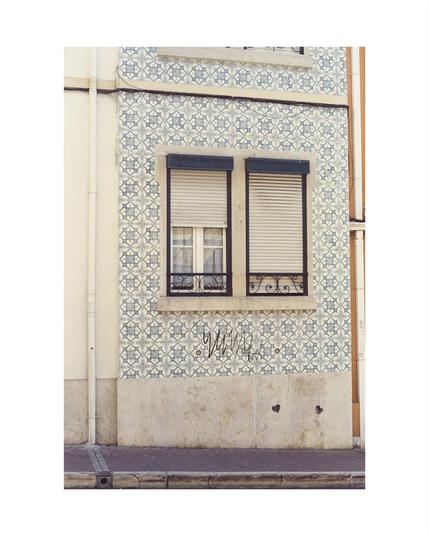 house with tiled facade in white and blue in a lisbon neighborhood, in the bottom third a big graffiti style signature