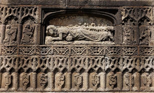 The granite exterior of a church profusely decorated with carvings, including one of St Mary Magdalene lying on her front with her pot of oil beside her.