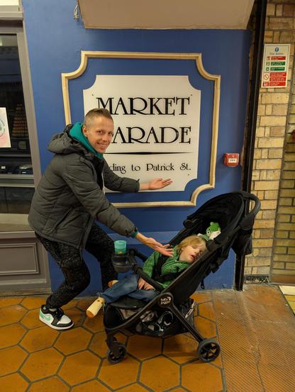 Patrick stands gesturing toward his son and to a sign that says "Patrick St." Taken in Cork, Ireland.