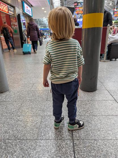 Patrick's son Patrick stands in a train station, facing away from the camera.