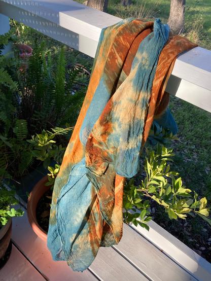 A blue and rust colored shawl draped over a railing in the sunset.