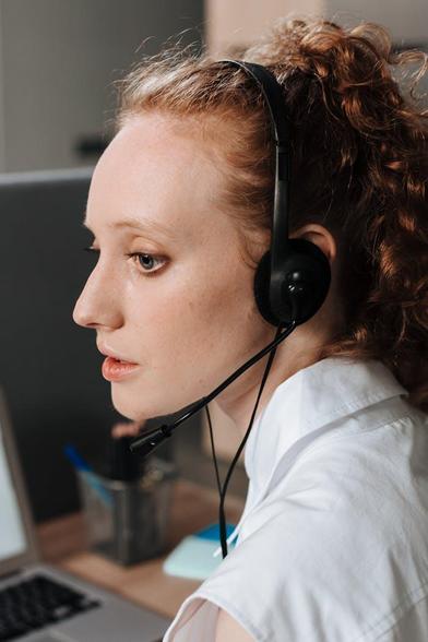A woman wearing a headset, focused on her laptop, engaged in a virtual meeting or online work
