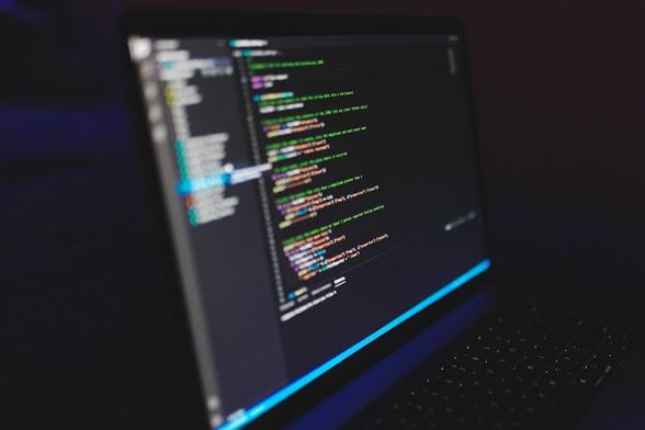 A laptop displaying lines of code on its screen, set against a neutral background