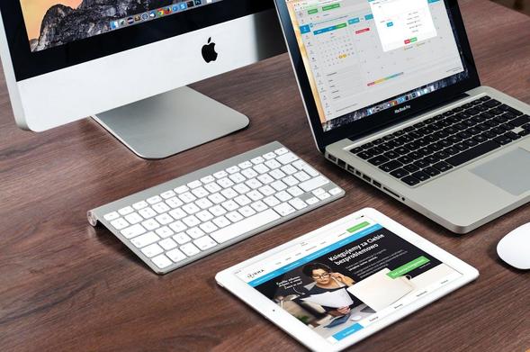 A laptop, tablet, and desktop computer arranged neatly on a wooden desk, showcasing a modern workspace setup