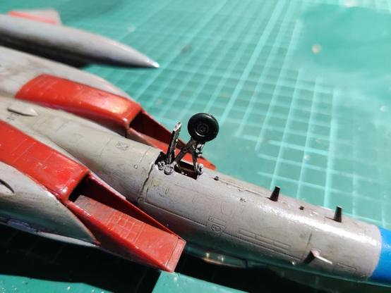 A reattached, badly broken front landing gear of an F-15E that looks more like a thing made up by an image generator than a real plane model. The wheel is glued onto the gear strut instead of the attachment point, as the proper part snapped off and was lost by cats.
