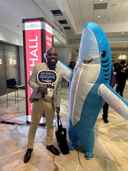 A man smiling and standing with Sharky in the CSUN conference lobby.